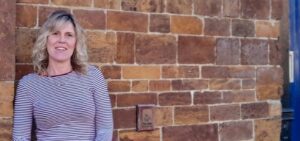 Woman in stripe top standing against brick wall smiling||