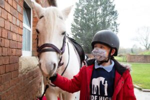 Young girl in red coat and make holding the reigns of a white horse|