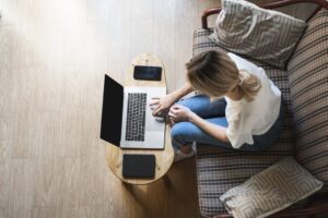 Woman is sitting on a sofa and using a laptop at wooden table. Study and work online